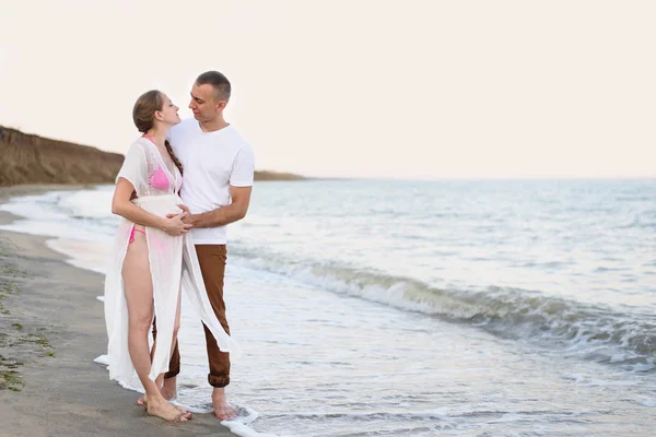 Молода подружня пара на морському узбережжі. Чоловік обіймає свою вагітну дружину. Pre-Sunset час — стокове фото