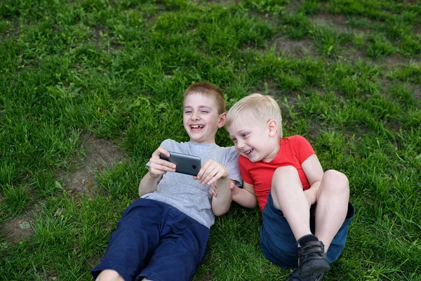 Két fiú egy okostelefon a kezükben a szórakozás a fűben — Stock Fotó