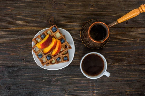 Schokolade belgische Waffeln mit Früchten, Tasse Kaffee und Cezve auf Holzuntergrund. leckeres Frühstück. Ansicht von oben — Stockfoto