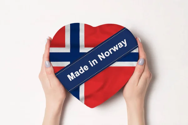 Inscripción Hecho en Noruega la bandera de Noruega. Manos femeninas sosteniendo una caja en forma de corazón. Fondo blanco . — Foto de Stock