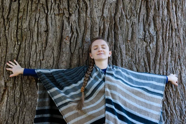 Молодая женщина прислонилась спиной к стволу большого дерева. Закрытые глаза. Единство с природой — стоковое фото