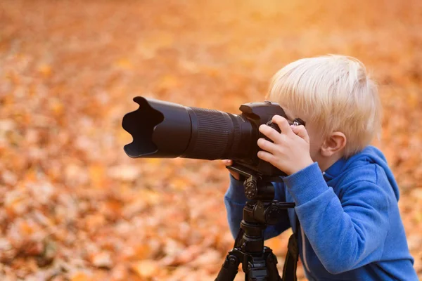 Malý blonďák fotografuje na SLR kameře. Podzimní Park — Stock fotografie