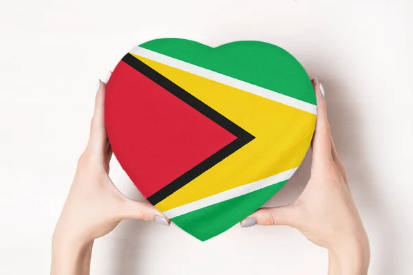 Bandera de Guyana en una caja en forma de corazón en manos femeninas. Fondo blanco — Foto de Stock