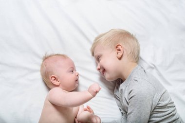 Bebek ve gülümseyen ağabeyi yatakta yatıyor. Oynarlar, iletişim kurarlar ve etkileşime girerler. Üstte görüntü
