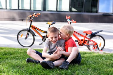 İki çocuk çimenlerin üzerinde otururken iletişim kuruyor. Bisikletten sonra dinlen, arka planda bisikletler