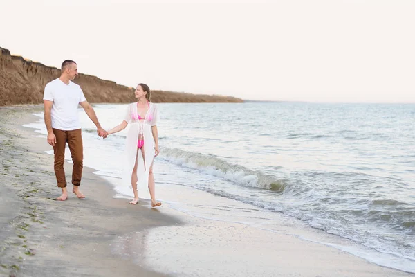 Νεαρό παντρεμένο ζευγάρι περπατά κατά μήκος της ακτής της θάλασσας. Εγκυμοσύνης. Χρόνος πριν το ηλιοβασίλεμα — Φωτογραφία Αρχείου