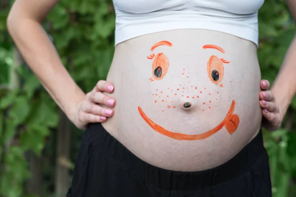 Vientre de una mujer embarazada con una cara sonriente pintada. Fondo verde — Foto de Stock