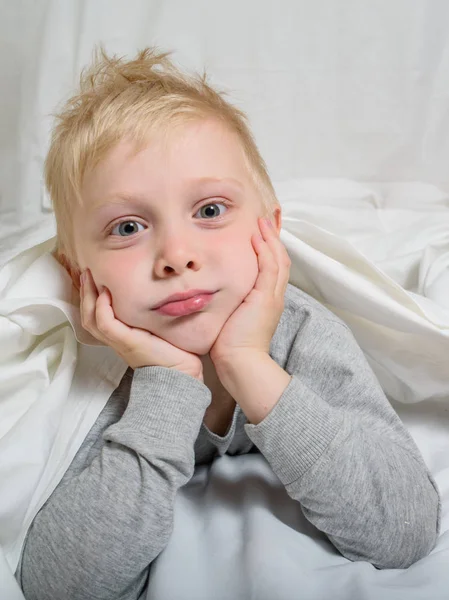 Vermoeide blonde jongen ligt met zijn hoofd in zijn handen. Witte achtergrond — Stockfoto