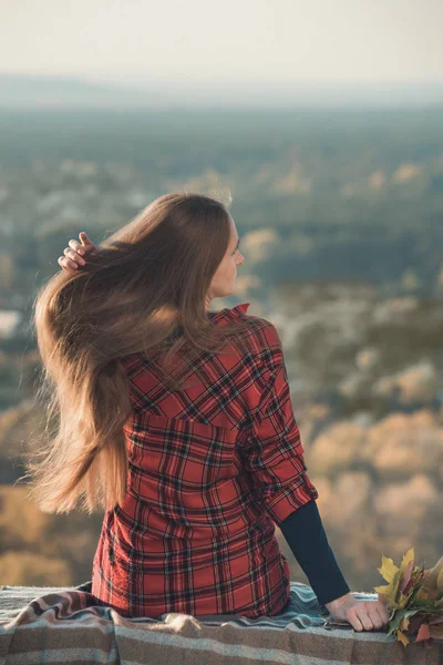 Young woman straightens a long hair sits on a hill overlooking the village. Back view — Stock Photo, Image