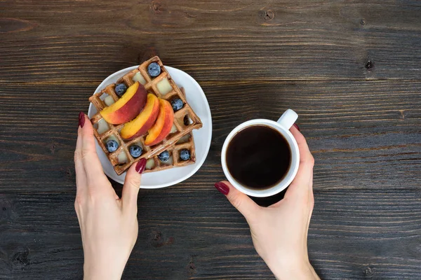 Belgische Waffeln mit Früchten und Beeren. weibliche Hand mit Tasse Kaffee. Holzuntergrund. Ansicht von oben — Stockfoto