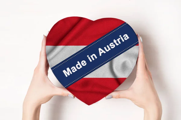 Επιγραφή Made in Αυστρία η σημαία της Αυστρίας. Γυναικεία χέρια που κρατάνε ένα κουτί σε σχήμα καρδιάς. Λευκό φόντο. — Φωτογραφία Αρχείου