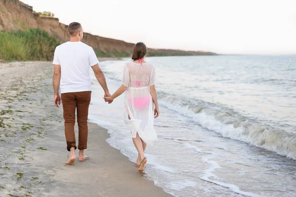 Το νεαρό ζευγάρι περπατάει στα χέρια κατά μήκος της θαλάσσιας ακτής. Πίσω όψη — Φωτογραφία Αρχείου