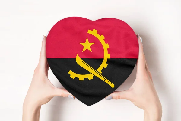 Σημαία της Αγκόλας σε κουτί σε σχήμα καρδιάς σε γυναικεία χέρια. Λευκό φόντο — Φωτογραφία Αρχείου