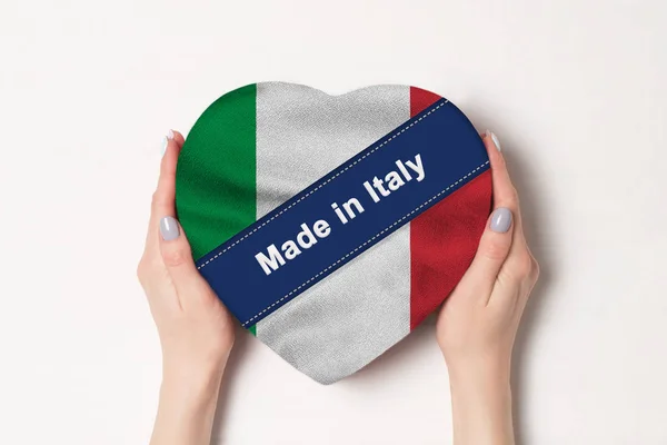 Felirat Made in Italy the flag of Italy. A női kezek egy szív alakú dobozt tartanak. Fehér háttér. — Stock Fotó