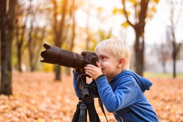 小さなブロンドの男の子は、一眼レフカメラで写真を撮ります。秋の公園 — ストック写真