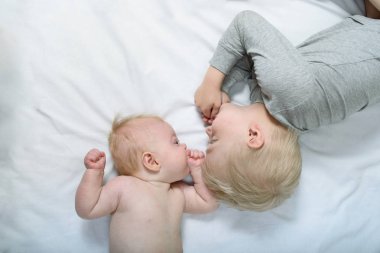 Bebek ve gülümseyen ağabeyi yatakta yatıyor. Komik ve etkileşimli. Üstte görüntü