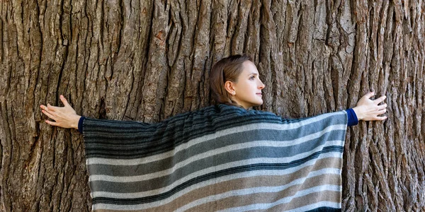 Mujer joven abrazando el tronco de un árbol grande. Unidad con la naturaleza, bosque otoñal — Foto de Stock