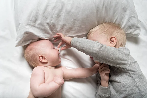 Baby och leende äldre bror ligger på sängen. De leker, rolig och interagerar. Uppifrån och — Stockfoto