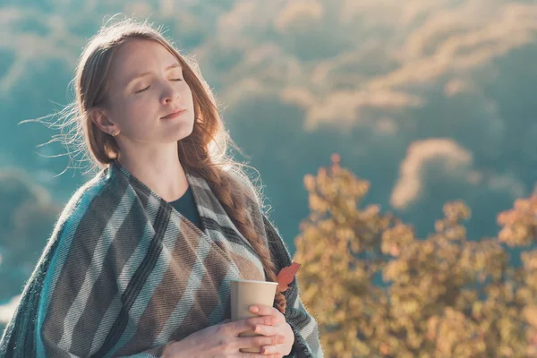 Молода жінка з закритими очима насолоджується повітрям. Паперова чашка в руках, сонячний день — стокове фото
