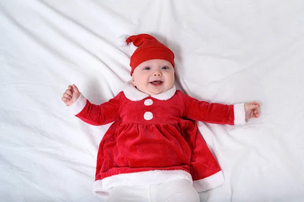 Porträtt av leende liten flicka i tomte hatt och en röd klänning. Ligger på vit bakgrund. Julkoncept — Stockfoto