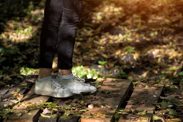 Pies de mujer en zapatillas blancas en un puente de madera. Parque de otoño sobre un fondo — Foto de Stock