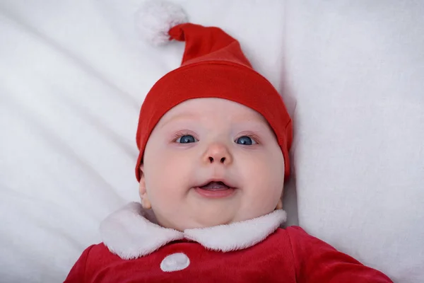 Portret uroczego maluszka w kapeluszu Mikołaja. Leżąc na białym tle. — Zdjęcie stockowe