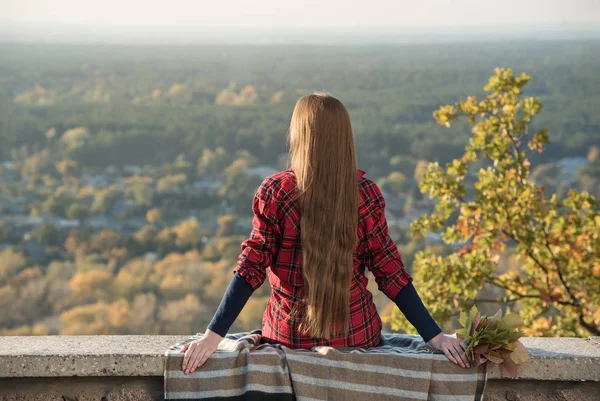 Young woman with long hair sits on a hill overlooking the village. Back view — Stock Photo, Image