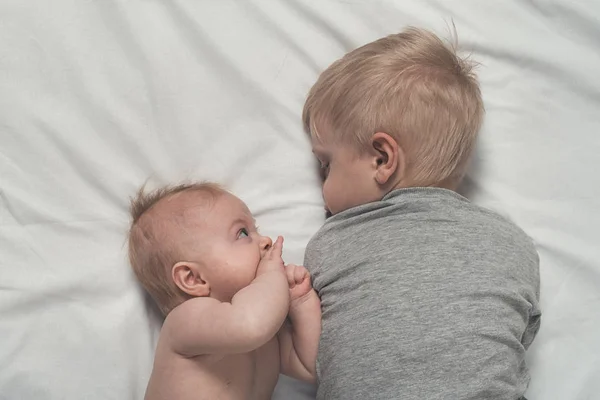 Bebé y hermano mayor sonriente están acostados en la cama. Juegan, se comunican e interactúan. Vista superior —  Fotos de Stock