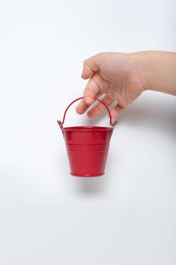 Beyaz arka planda çocukların elinde küçük kırmızı bir kova.