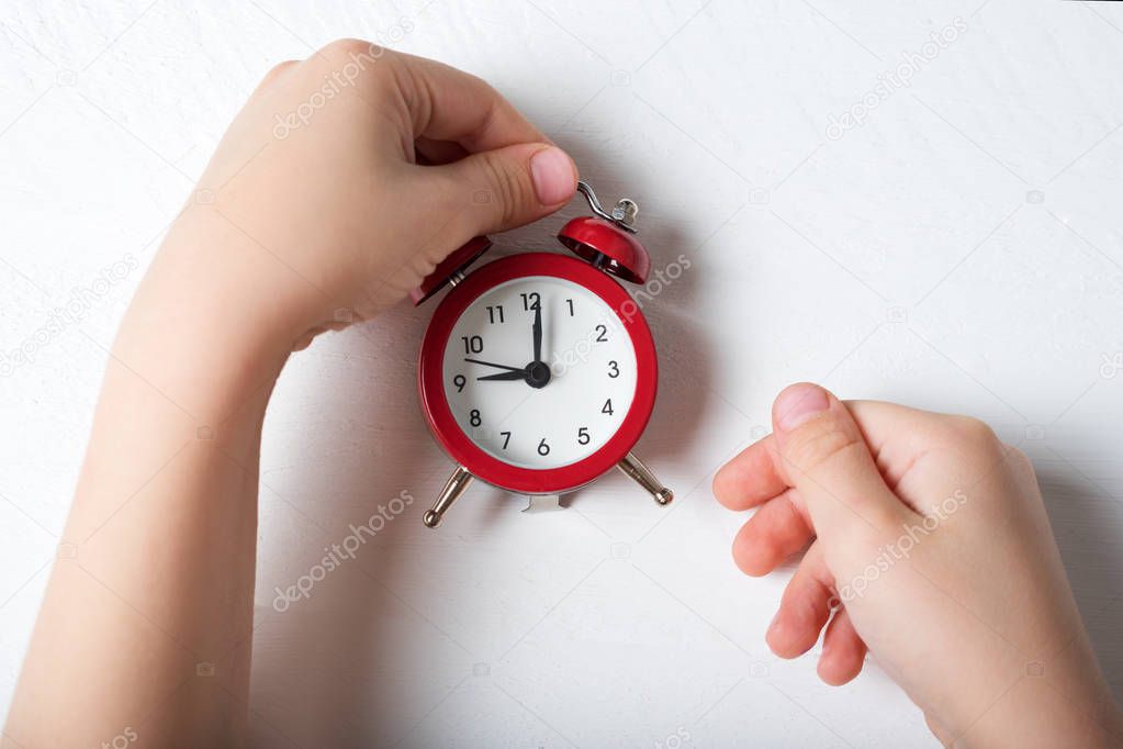 Red alarm clock in children's hands on a white background