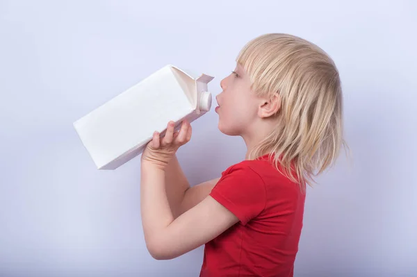 fair-haired boy drinking milk or juice from large carton. Portrait of child with carton of milk on white background.