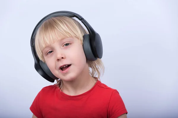 白い背景にヘッドフォンでブロンドの少年の肖像画 子供は音楽を聴く — ストック写真