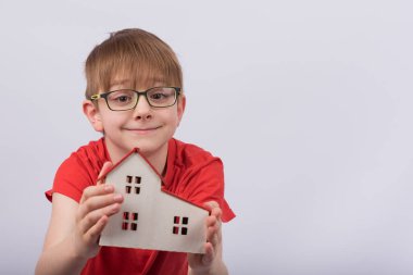 Beyaz arka planda evin modelini tutan çocuk. Gözlüklü sevimli çocuk oyuncak evi tutuyor. evde eğitim.