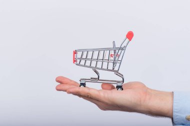 Erkek avucunda küçük bir alışveriş arabası, beyaz arkaplan. Oyuncak market arabası. Yan görünüm.