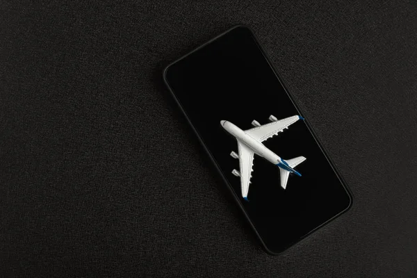 Model airplane on smartphone on black background. Application for searching airtickets