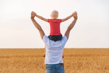 Oğlum, ellerim havada, babasının omuzlarında oturuyor. Mutlu çocukluk ve babalık.