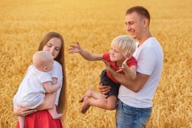 Genç ebeveynler ve iki çocuk dışarıda eğleniyorlar. Mutlu aile buğday tarlasında yürüyor