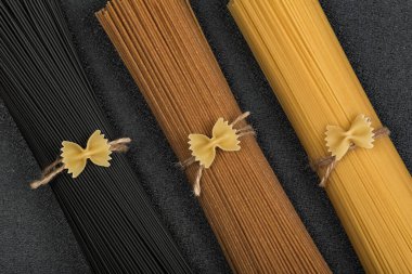 Gri arka planda siyah, kahverengi ve sarı spagetti. İtalyan malzemeleri. Yakın çekim..