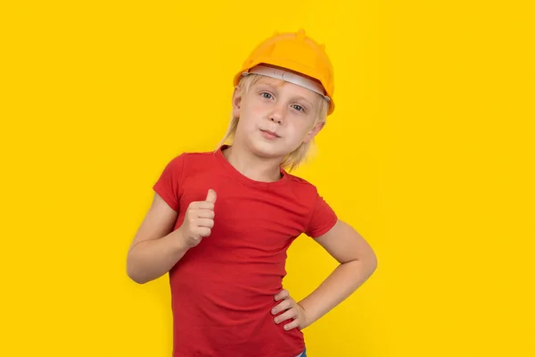 严肃的少年男孩戴着保护橙色的硬礼帽 表现出很好的手势 黄色背景的儿童 — 图库照片