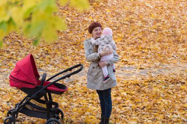 Sonbahar Parkı 'nda kucağında bebek taşıyan mutlu genç bir anne. Anne ve bebek arabası..