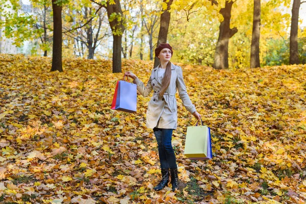 秋の公園の背景に手にショッピングバッグを持つ若い女性 秋の割引 — ストック写真