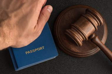 Male hand holds passport next to wooden gavel. Obtain citizenship. Legal immigration clipart