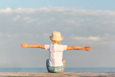 Hasır şapkalı çocuk denizde ve gökyüzünde oturuyor. Yaz tatilinde deniz tatili.