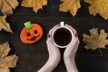 Kadın ellerinde çay fincanı ve tahta arka planda Cadılar Bayramı kurabiyeleri. Sonbahar yaprakları