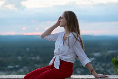 Genç ve güzel bir kadın panoramik platformda oturur ve elleriyle saçlarını düzeltir. Şık bir kadının portresi..