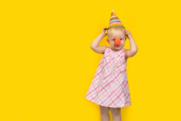 Kleines Mädchen Mit Partyhut Und Roter Clownsnase Auf Gelbem Hintergrund — Stockfoto