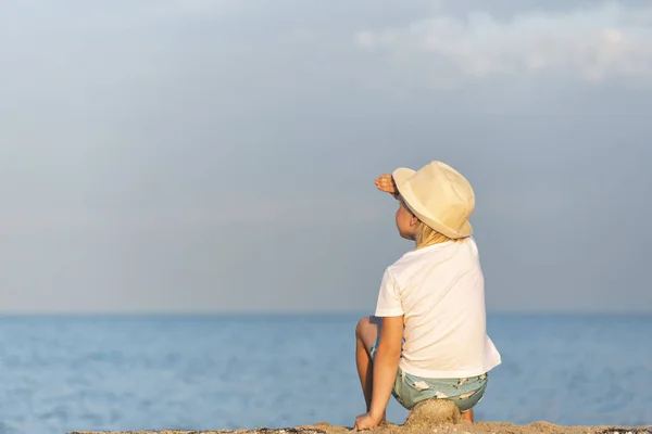 Hasır Şapkalı Çocuk Gün Batımında Sahilde Oturuyor Denize Bakıyor — Stok fotoğraf