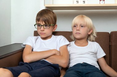 İki arkadaş kanepede oturuyor ve bir şeye bakıyorlar. İki kardeş kanepede oturuyor..