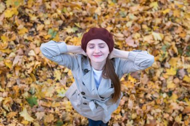 Düşen yaprakların üzerinde bereli güzel bir kız manzarası. Güz Parkı 'ndaki genç kadın.
