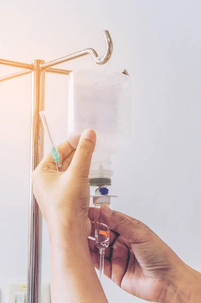 Nurse\'s hands is removing IV fluid drip from metal stand in hospital